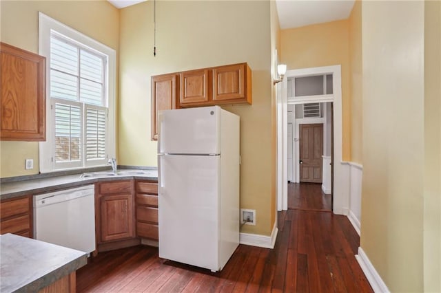 kitchen featuring white appliances, brown cabinets, dark wood finished floors, and a sink