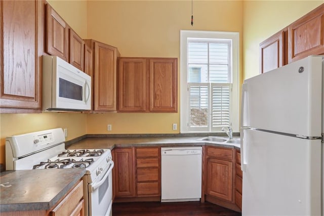 kitchen with dark countertops, white appliances, brown cabinets, and a sink