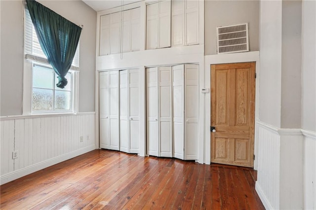 unfurnished bedroom featuring a wainscoted wall, hardwood / wood-style floors, and two closets