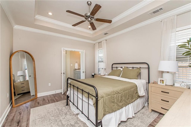 bedroom with a tray ceiling, visible vents, ornamental molding, wood finished floors, and baseboards