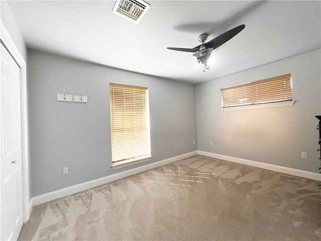 carpeted empty room with baseboards, visible vents, and a ceiling fan