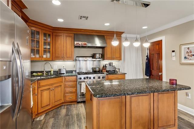 4701 Lake Vista Dr, Metairie, LA 70006 - kitchen featuring stainless steel appliances, wall chimney exhaust hood, dark wood-style floors, brown cabinets, and glass insert cabinets