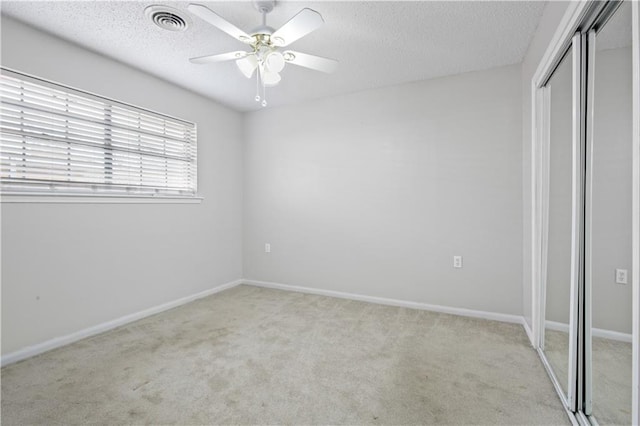 unfurnished bedroom featuring a closet, visible vents, light carpet, a textured ceiling, and baseboards