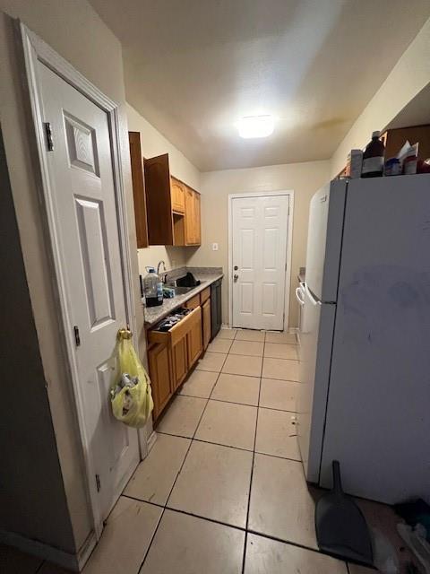 kitchen featuring brown cabinets, freestanding refrigerator, light countertops, a sink, and light tile patterned flooring