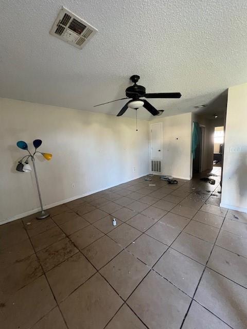 empty room featuring a ceiling fan, visible vents, a textured ceiling, and light tile patterned floors