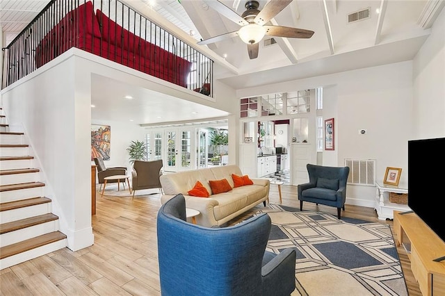 living area featuring a towering ceiling, light wood-style flooring, and visible vents