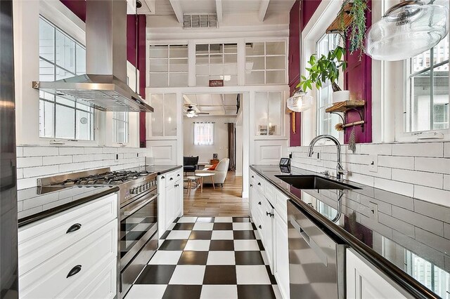 kitchen with appliances with stainless steel finishes, dark countertops, island exhaust hood, and a sink