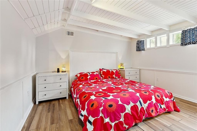 bedroom with lofted ceiling with beams, a wainscoted wall, wood finished floors, wood ceiling, and visible vents