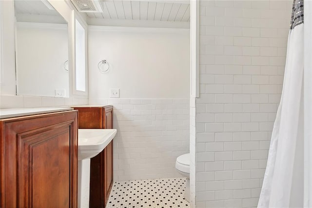 bathroom featuring a wainscoted wall, tile walls, visible vents, vanity, and tiled shower