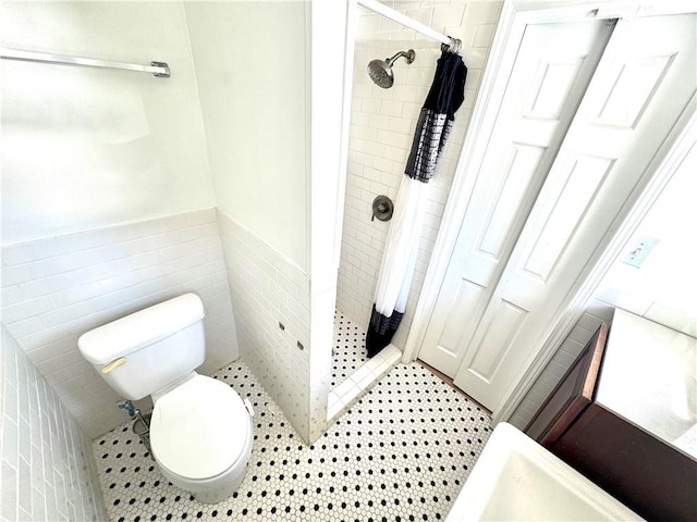 bathroom featuring wainscoting, toilet, tile patterned flooring, a shower stall, and tile walls