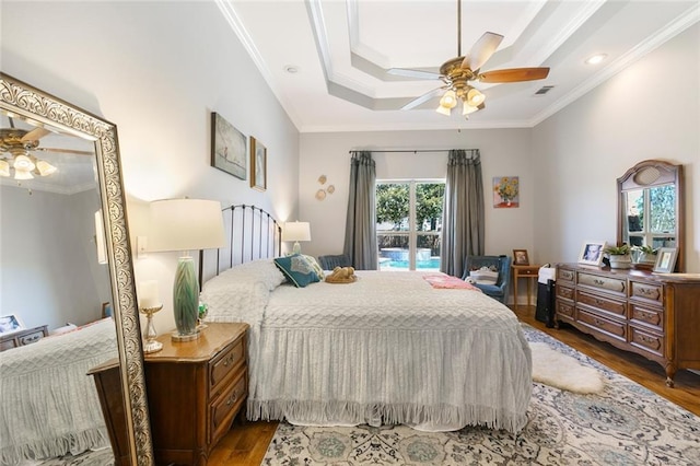 bedroom with a tray ceiling, visible vents, crown molding, and wood finished floors