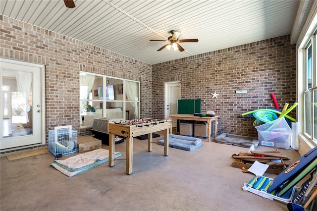 recreation room featuring brick wall, ceiling fan, and concrete flooring