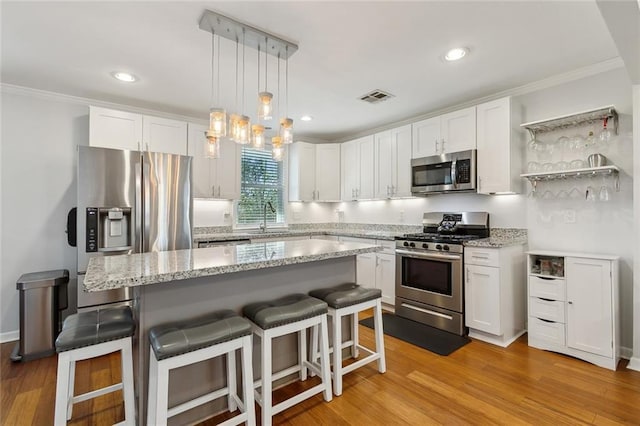 kitchen featuring stainless steel appliances, visible vents, a kitchen breakfast bar, and white cabinetry