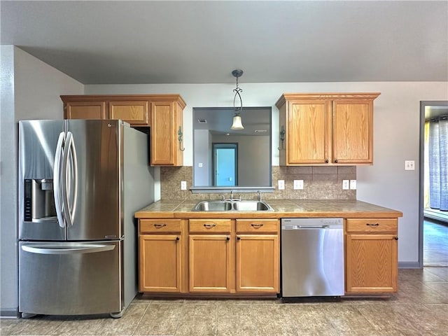 kitchen featuring a sink, appliances with stainless steel finishes, backsplash, brown cabinets, and decorative light fixtures