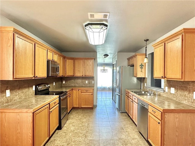 kitchen with tile counters, appliances with stainless steel finishes, a sink, and visible vents