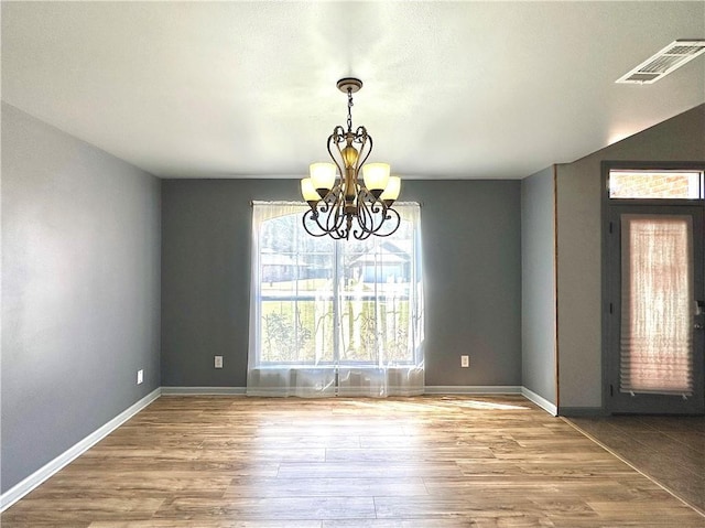 unfurnished dining area with a chandelier, visible vents, baseboards, and wood finished floors