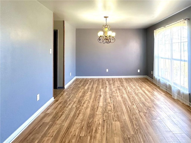 unfurnished room featuring a chandelier, baseboards, and wood finished floors