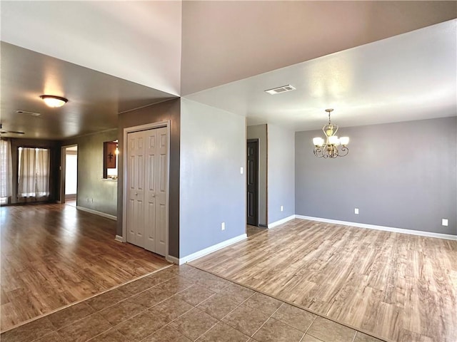 empty room featuring baseboards, visible vents, an inviting chandelier, and wood finished floors