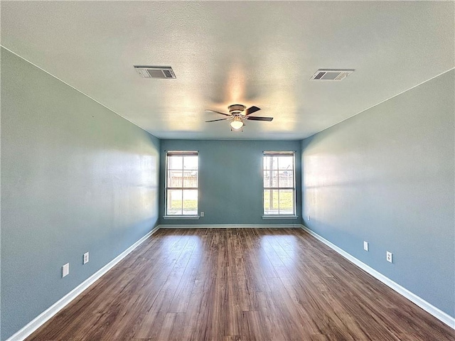 unfurnished room featuring dark wood-style floors, visible vents, baseboards, and a ceiling fan