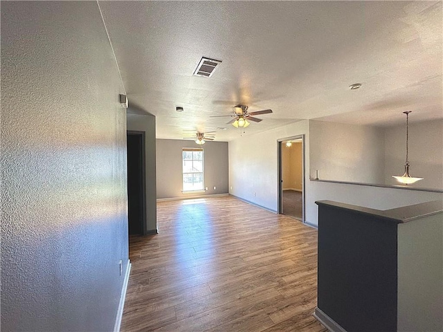 unfurnished room with baseboards, visible vents, a ceiling fan, wood finished floors, and a textured ceiling