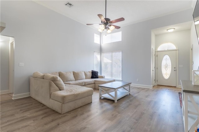 living area featuring baseboards, light wood-type flooring, visible vents, and crown molding