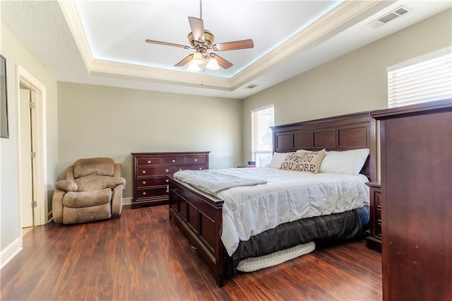 bedroom with visible vents, dark wood finished floors, baseboards, ceiling fan, and a tray ceiling