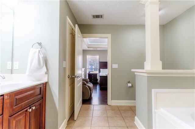 ensuite bathroom featuring a textured ceiling, tile patterned flooring, visible vents, vanity, and ornate columns