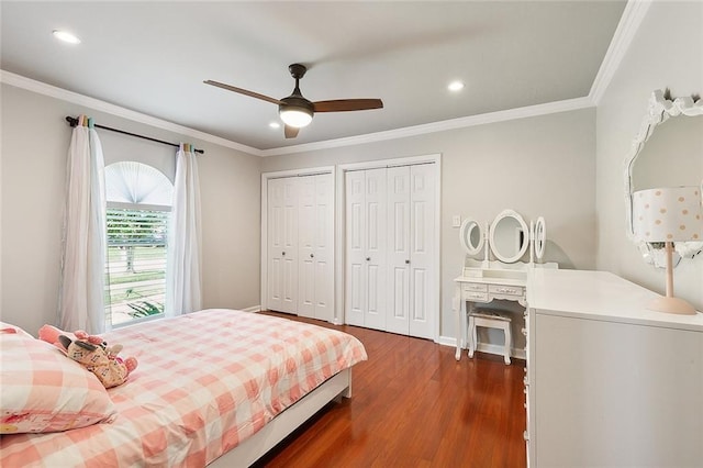 bedroom with dark wood-style flooring, two closets, and crown molding