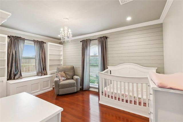 bedroom featuring crown molding, dark wood finished floors, a crib, and an inviting chandelier