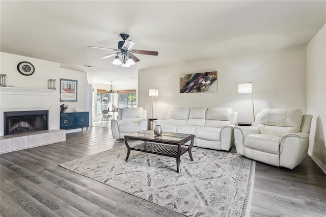 living room featuring a tiled fireplace, baseboards, wood finished floors, and ceiling fan with notable chandelier