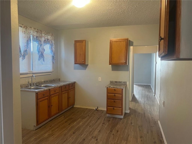 kitchen with a sink, dark wood-type flooring, brown cabinetry, and a textured ceiling