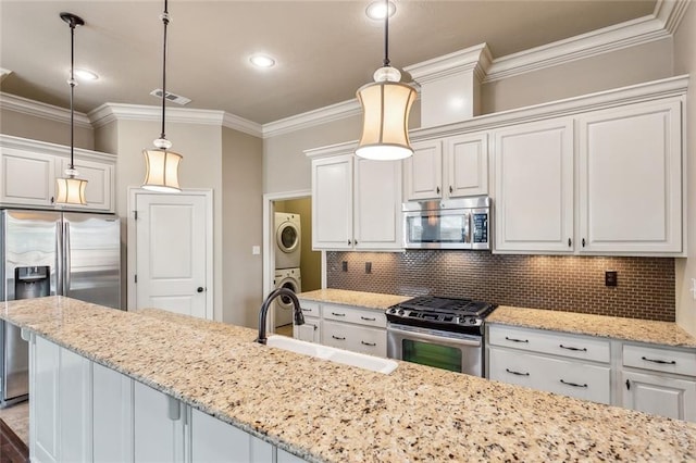 kitchen with stainless steel appliances, stacked washer and dryer, a sink, decorative backsplash, and light stone countertops