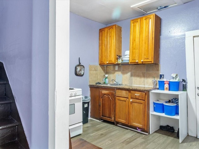 kitchen with brown cabinets, light wood finished floors, tasteful backsplash, white range with gas cooktop, and a sink