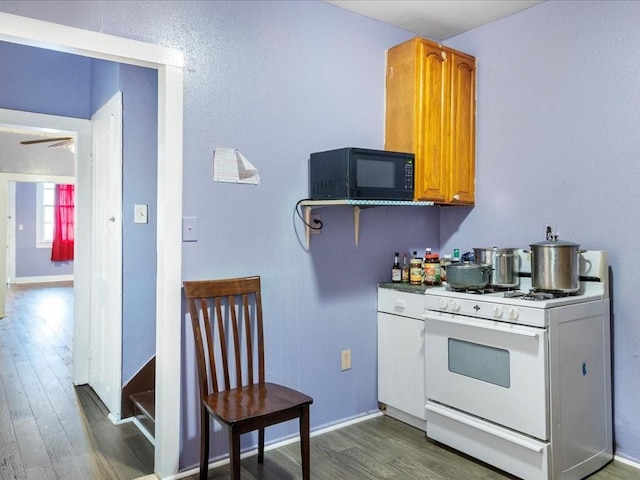 kitchen featuring baseboards, brown cabinetry, dark wood finished floors, white gas stove, and black microwave