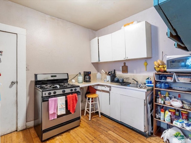 kitchen featuring light wood finished floors, white cabinetry, light countertops, and stainless steel range with gas stovetop