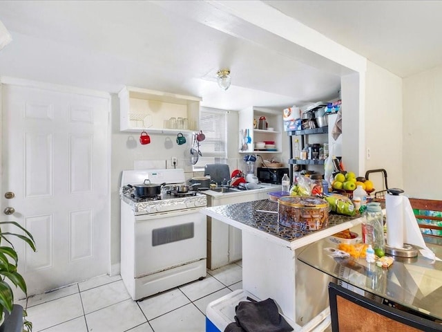 kitchen featuring black microwave, open shelves, light tile patterned flooring, and white range with gas stovetop