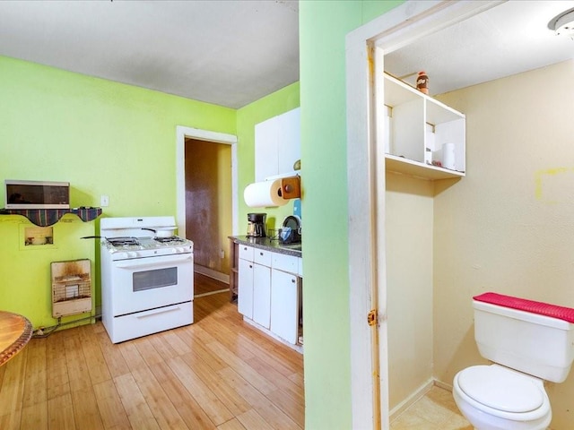 kitchen featuring light wood finished floors, baseboards, white cabinets, dark countertops, and gas range gas stove