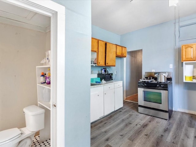 kitchen with light wood-type flooring, stainless steel gas range, black microwave, and light countertops