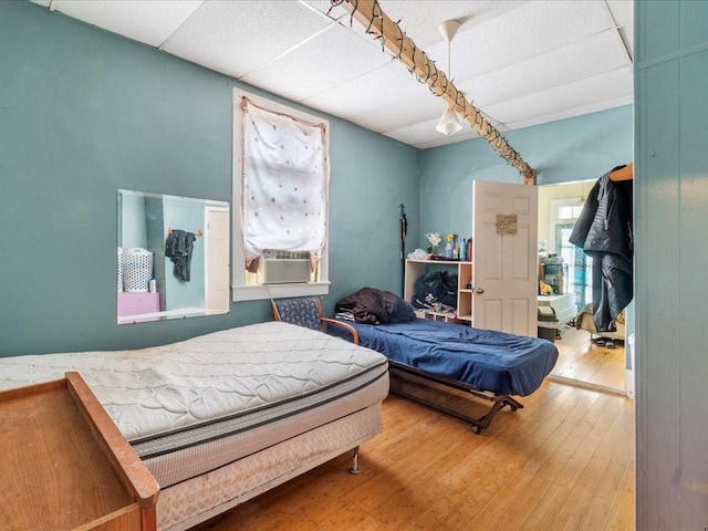 bedroom with hardwood / wood-style floors, cooling unit, and a paneled ceiling