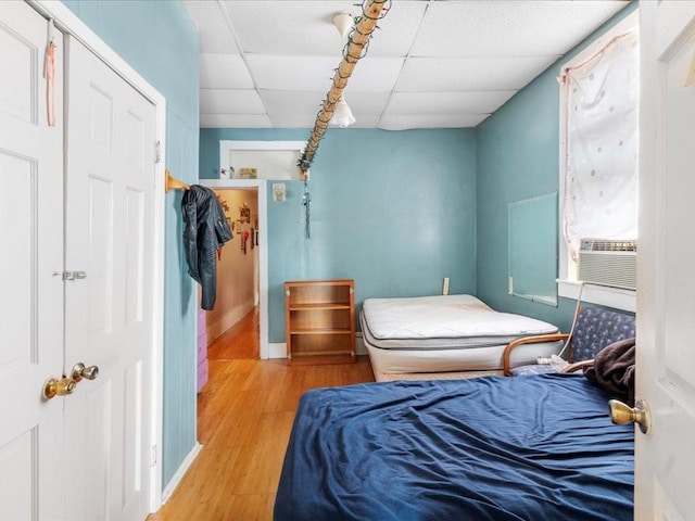 bedroom with cooling unit, a drop ceiling, and wood finished floors