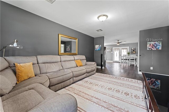 living room featuring a ceiling fan, visible vents, baseboards, and wood finished floors