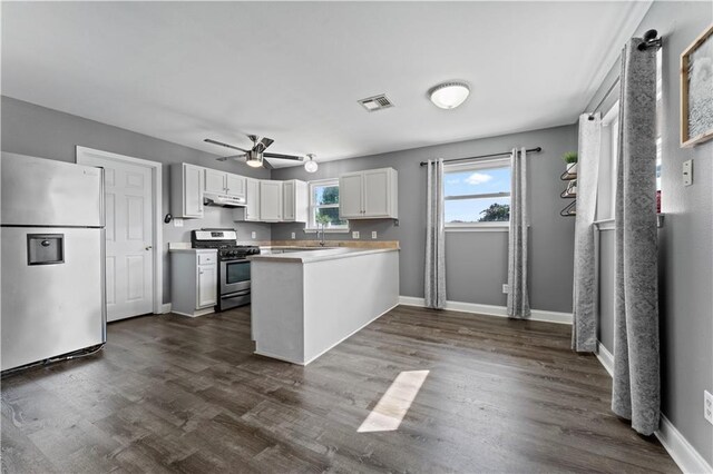 kitchen featuring stainless steel appliances, a peninsula, dark wood-style flooring, visible vents, and baseboards