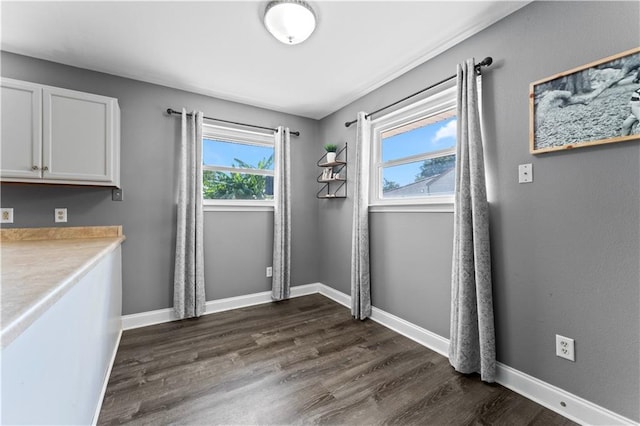 unfurnished dining area with dark wood-style floors and baseboards