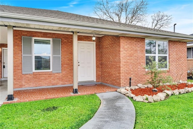 property entrance featuring a yard, brick siding, and roof with shingles