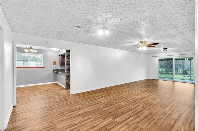 empty room featuring visible vents, baseboards, light wood-style flooring, a textured ceiling, and ceiling fan with notable chandelier