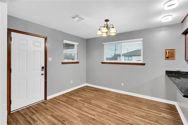 unfurnished dining area with light wood finished floors, baseboards, visible vents, and a notable chandelier