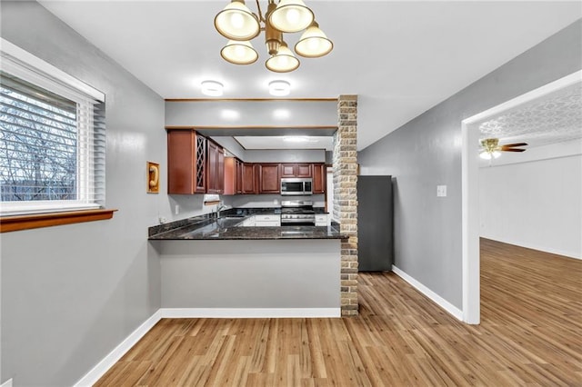 kitchen with ceiling fan with notable chandelier, stainless steel appliances, a peninsula, baseboards, and light wood-type flooring