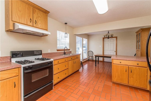 kitchen with under cabinet range hood, a sink, light countertops, gas range oven, and an inviting chandelier