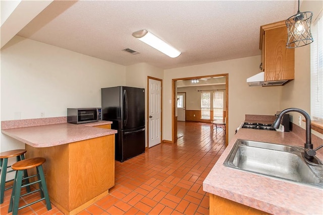 kitchen with brick floor, light countertops, freestanding refrigerator, a sink, and a peninsula