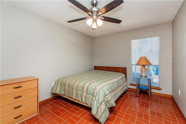 bedroom with ceiling fan, a textured ceiling, brick floor, and baseboards